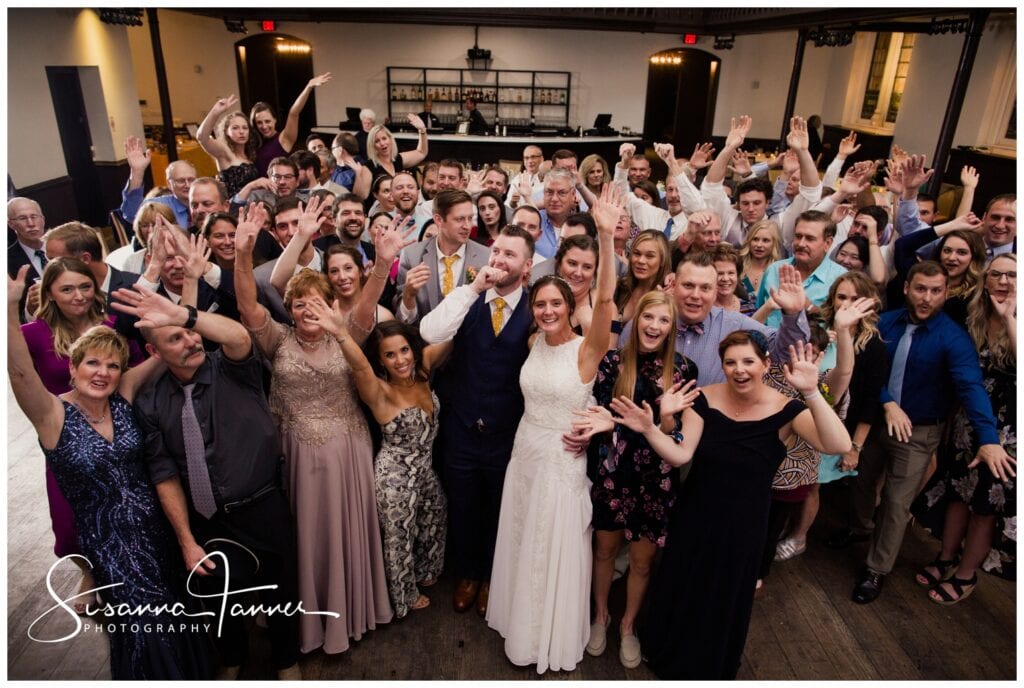 The Transept, Over-the-Rhine, Cincinnati Ohio wedding, full reception guest group shot with everyone waving. Bride and groom are front and center. 