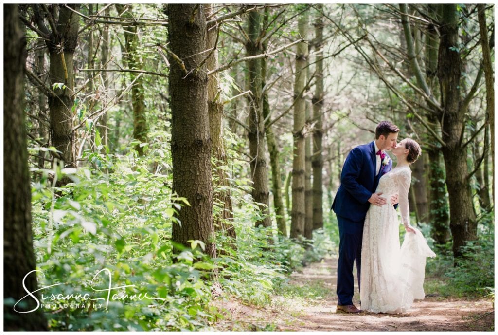 Cope Environmental Wedding Photography, couple kissing in the woods as she holds up the back of her dress