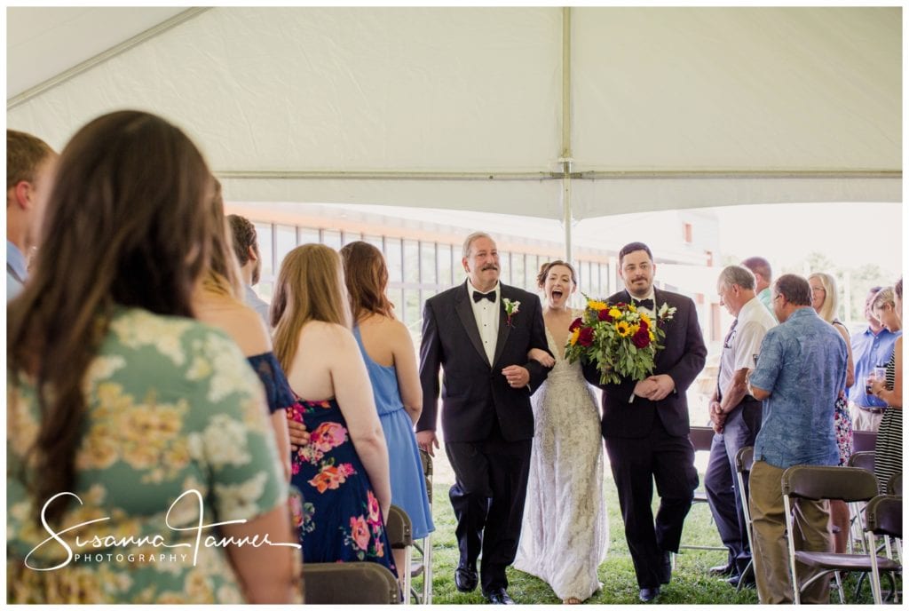 bride walking down aisle with father and brother with big smile on her face
