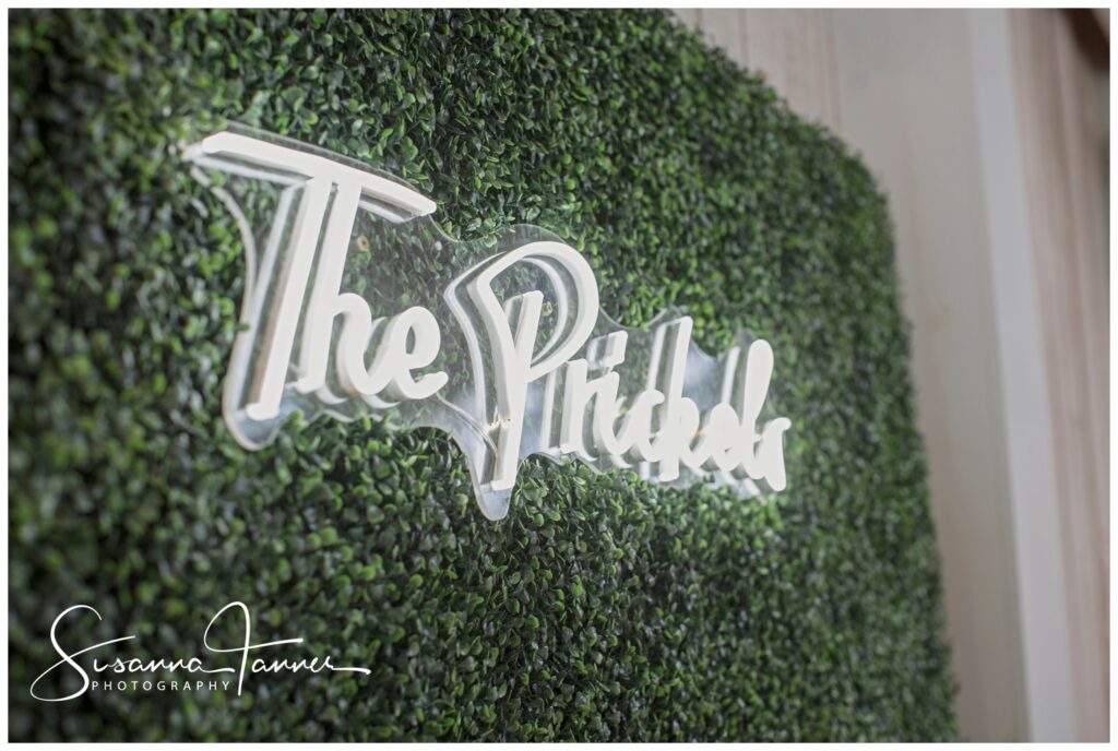 Venue wall decor with neon name of the couple over boxwood wall