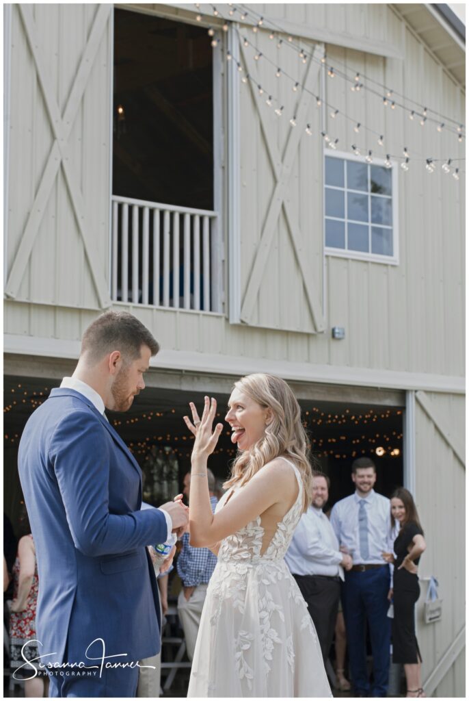 bride holding up her wedding ring hand and smiling while standing in front of Barn venue