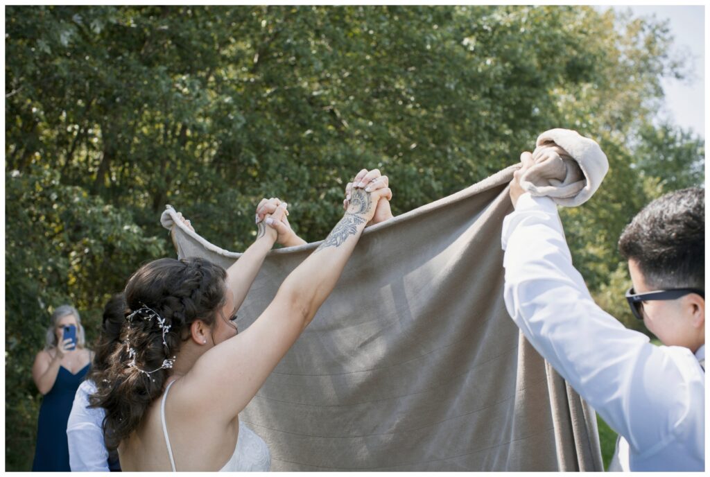 Gay wedding, west central Ohio, both brides hold hands above the held up blanket in preparation for their first look