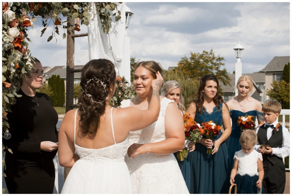 lesbian wedding, bride #2 lovingly adjusts bride #1 hair during the wedding ceremony
